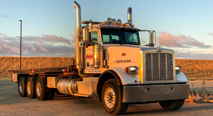 AAA Towing heavy-duty flatbed tow truck parked along an Alberta highway at sunset, exemplifying camper towing and door-to-destination service.